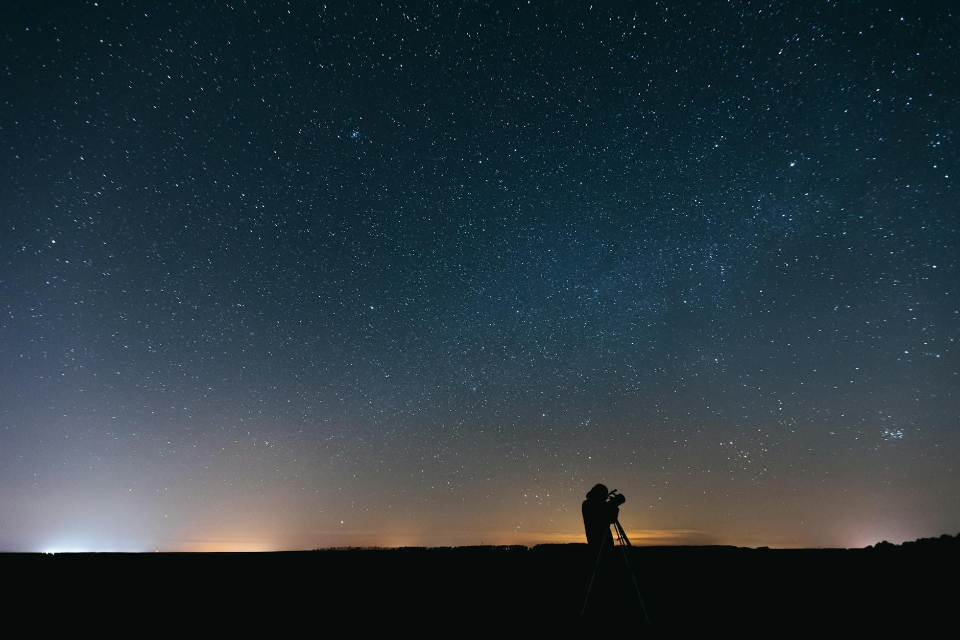 Osoba obserwująca nocne gwiazdy przez teleskop na tle rozgwieżdżonego nieba
